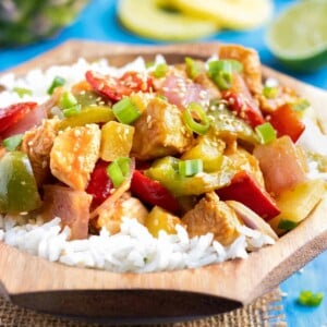 Pineapple chicken stir-fry in a wooden bowl with white rice.
