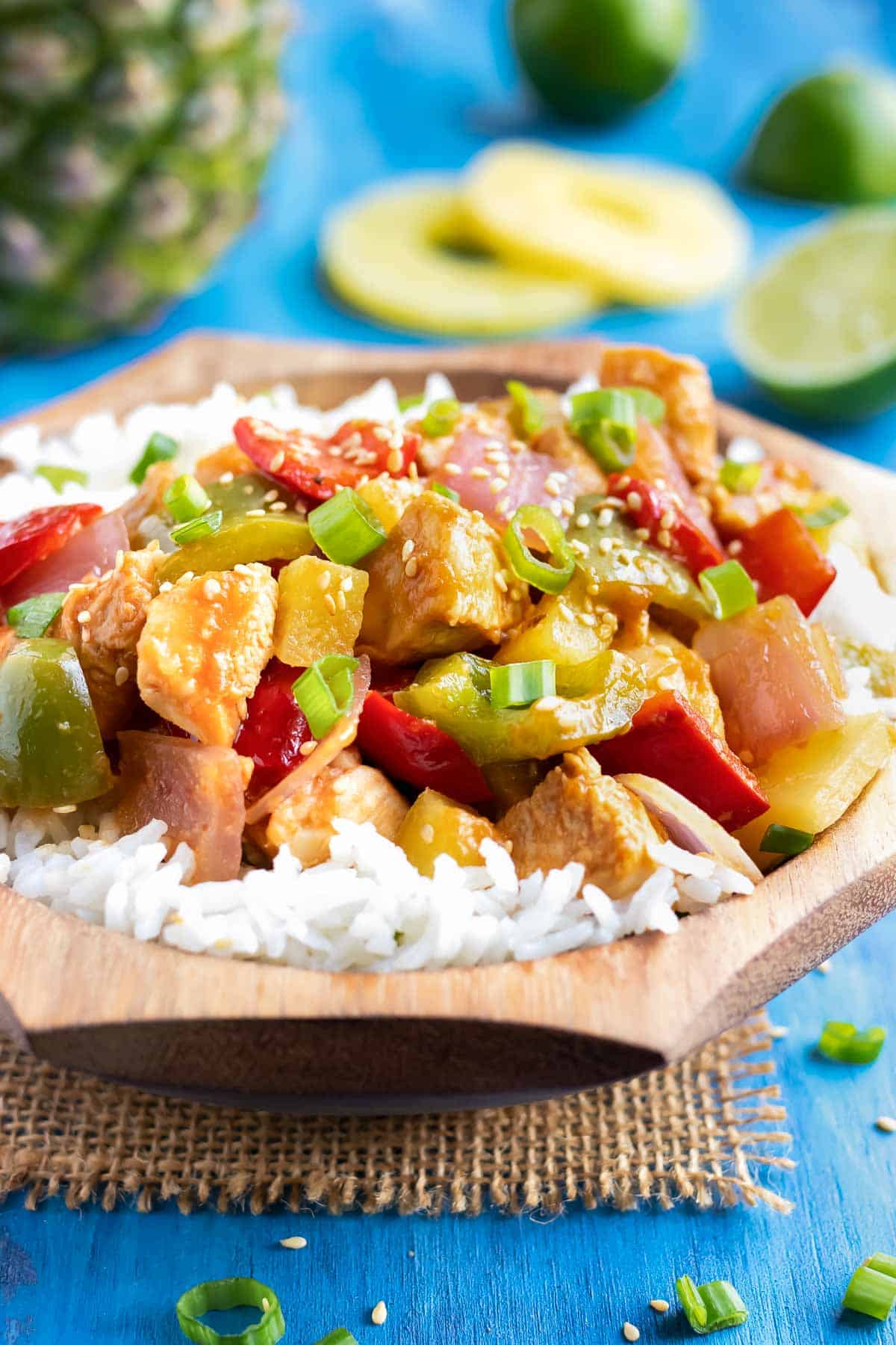 Pineapple chicken stir-fry in a wooden bowl with white rice.