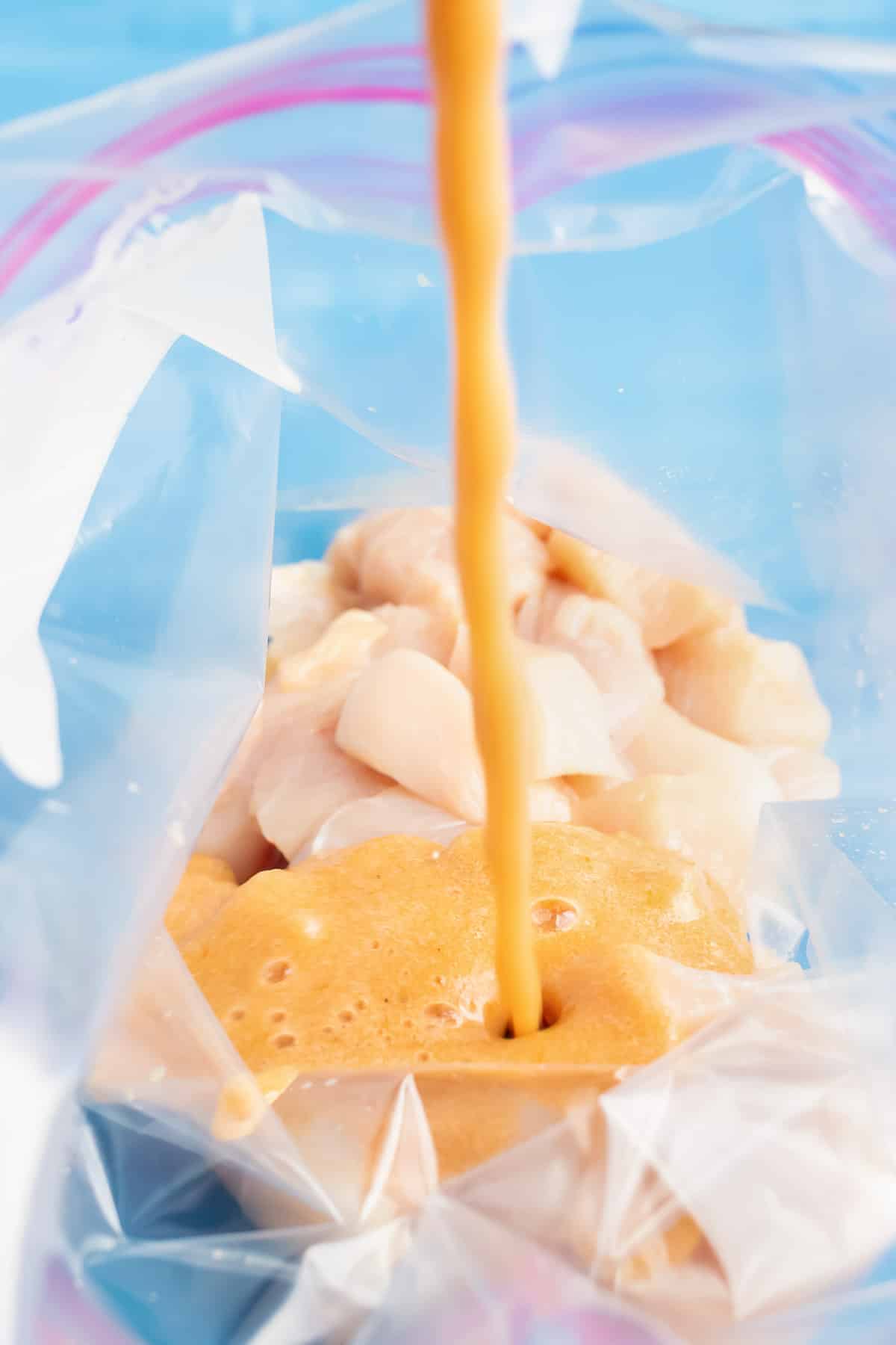 Marinade is poured over chicken in a bag.