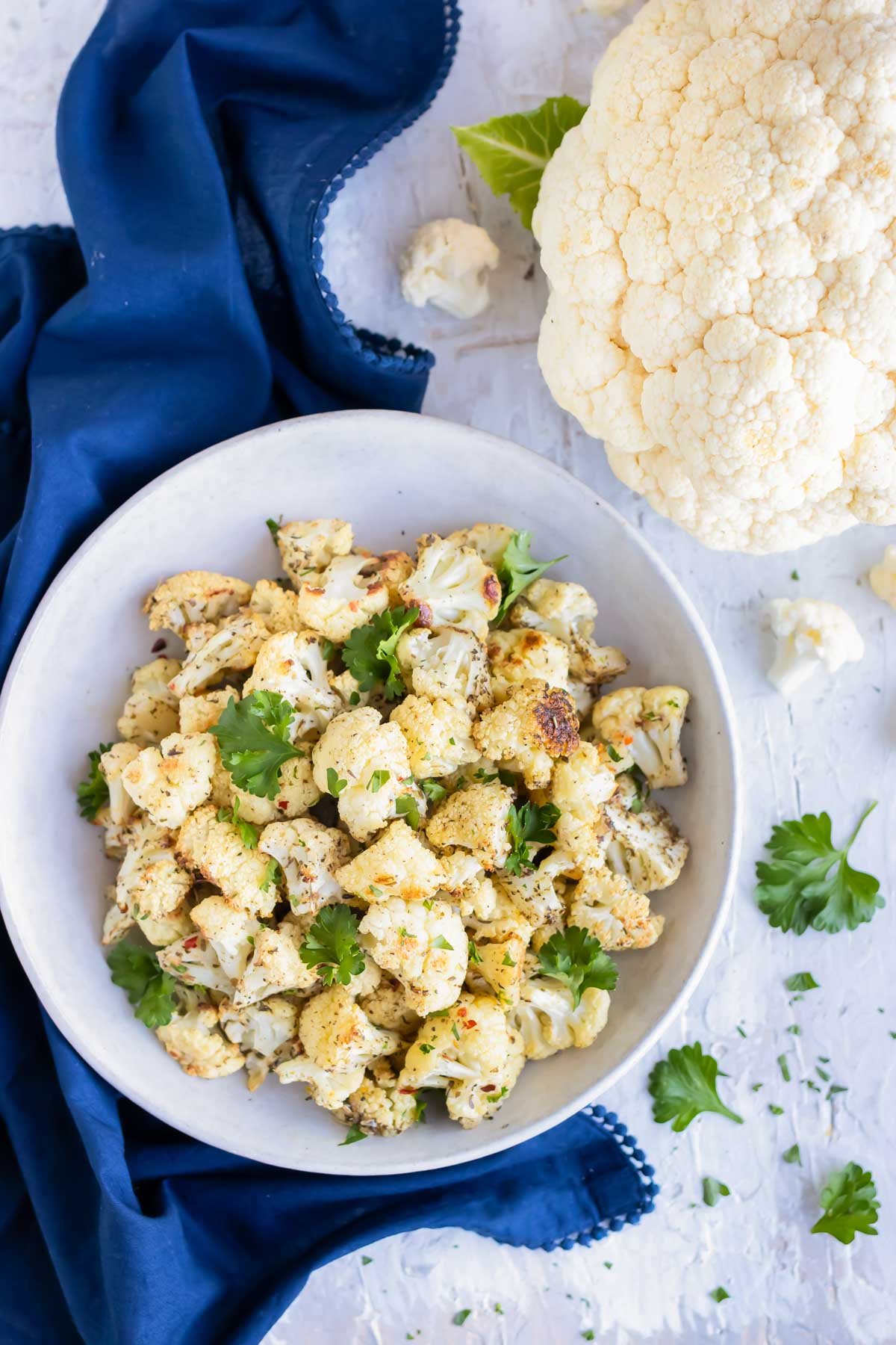 Oven-roasted cauliflower in a white bowl with a head of cauliflower on the side.