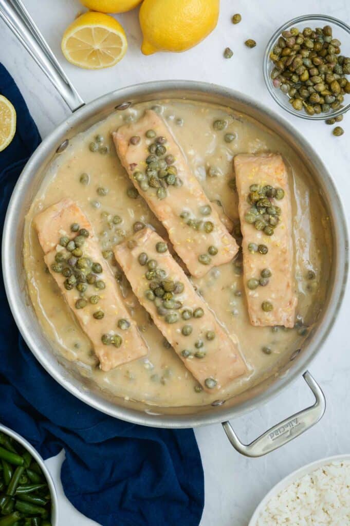 A skillet full of four salmon piccata filets.