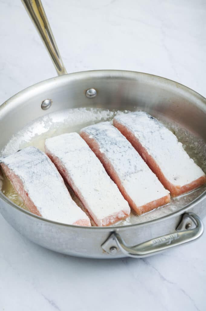 Salmon is cooked in a skillet with butter.