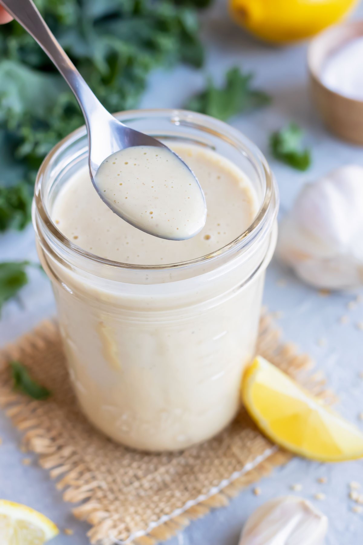 A spoon of creamy homemade vegan dressing being taken out of a jar full of lemon tahini dressing