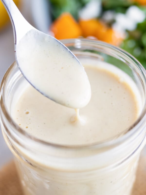 A close up of spoon of creamy homemade being taken out of a jar full of lemon tahini dressing