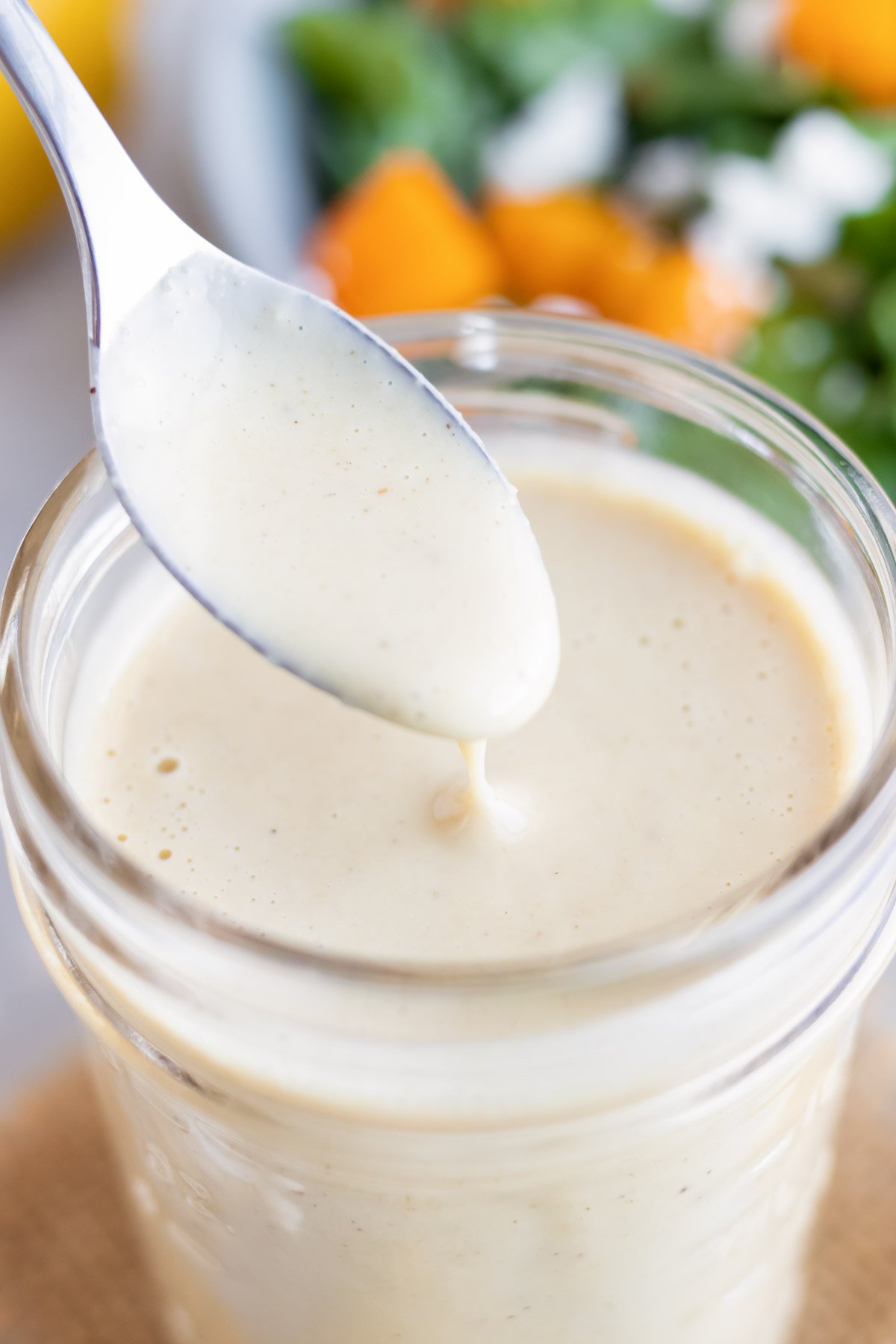 A close up of spoon of creamy homemade being taken out of a jar full of lemon tahini dressing
