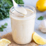 A spoon of creamy homemade being taken out of a jar full of lemon tahini dressing