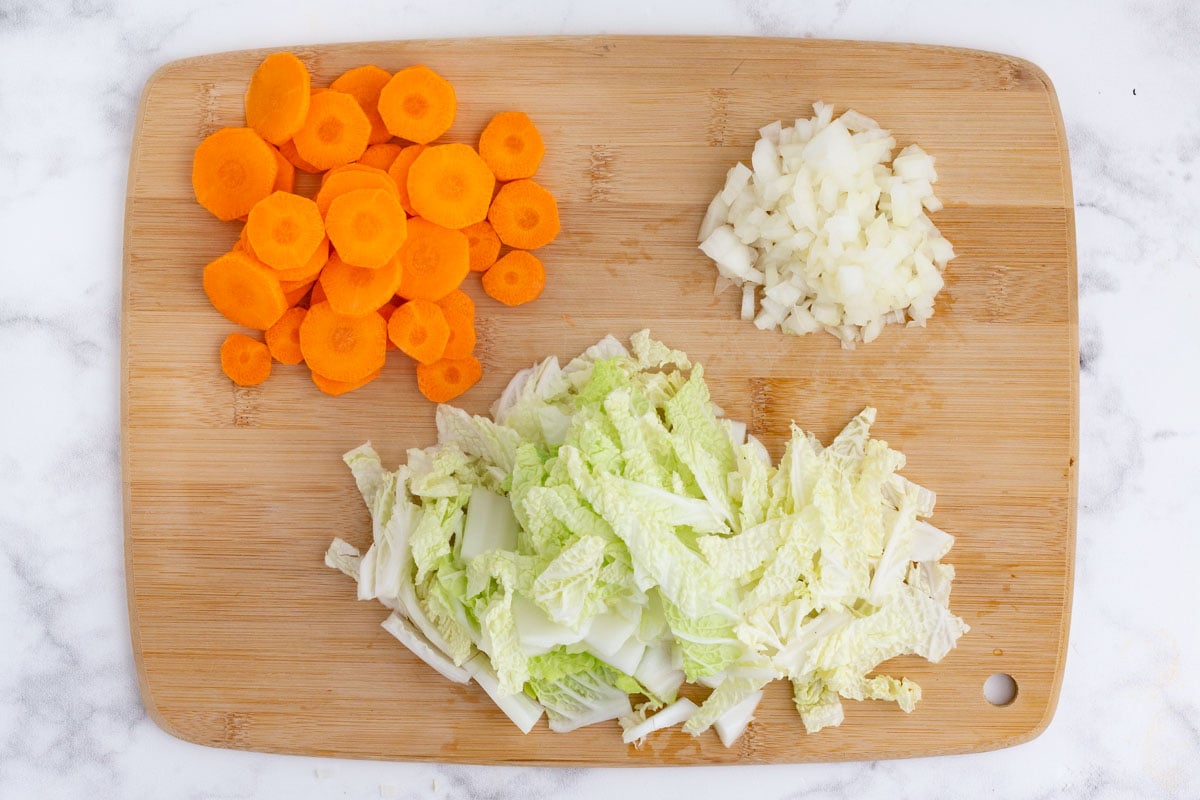 Chopped carrots, onion, and cabbage are on a cutting board.
