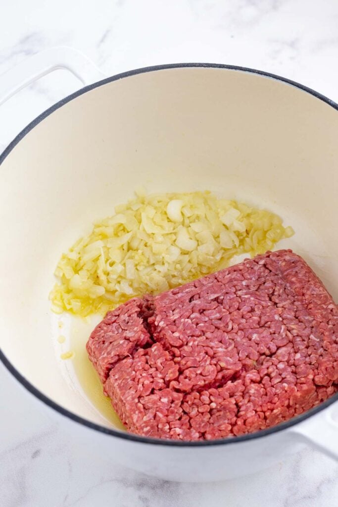 Ground beef is added to a pot with onion and garlic for a cabbage roll soup with rice.