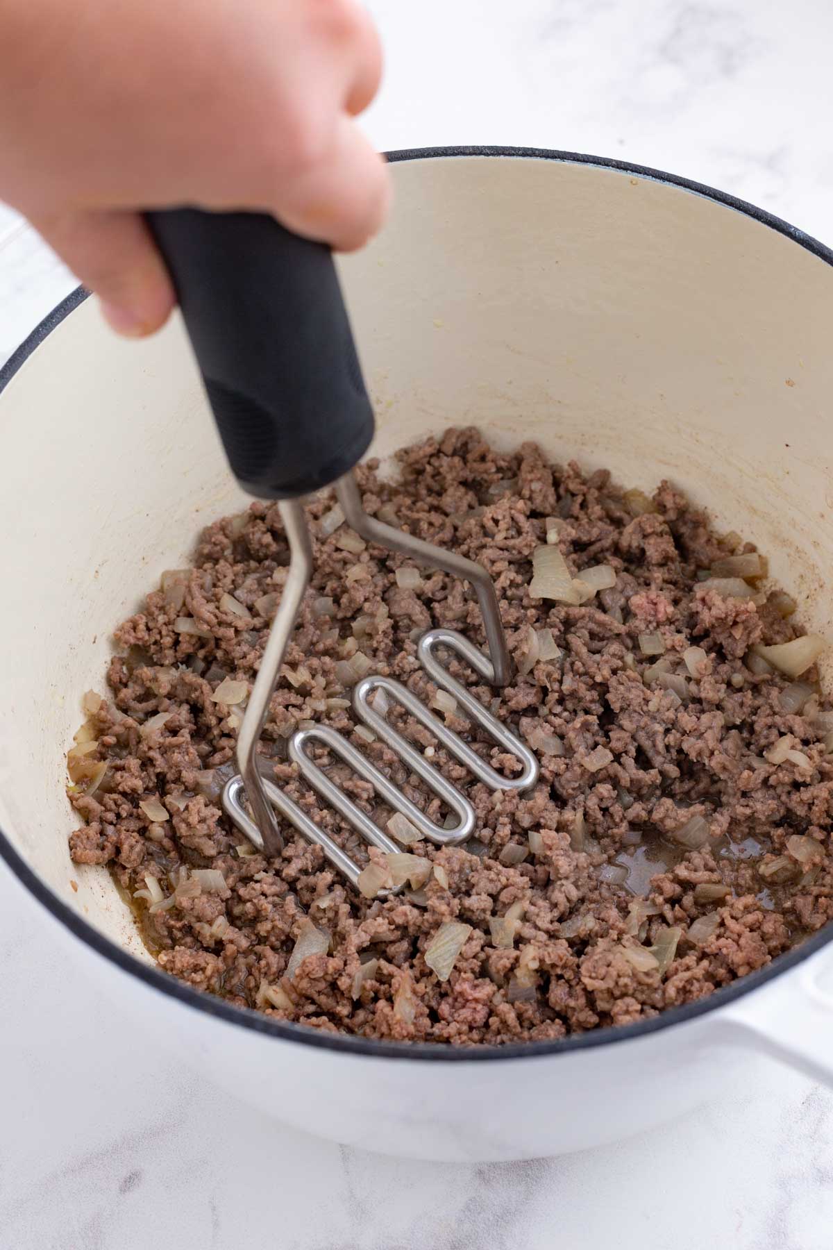 A meat masher crumbles the browned meat.