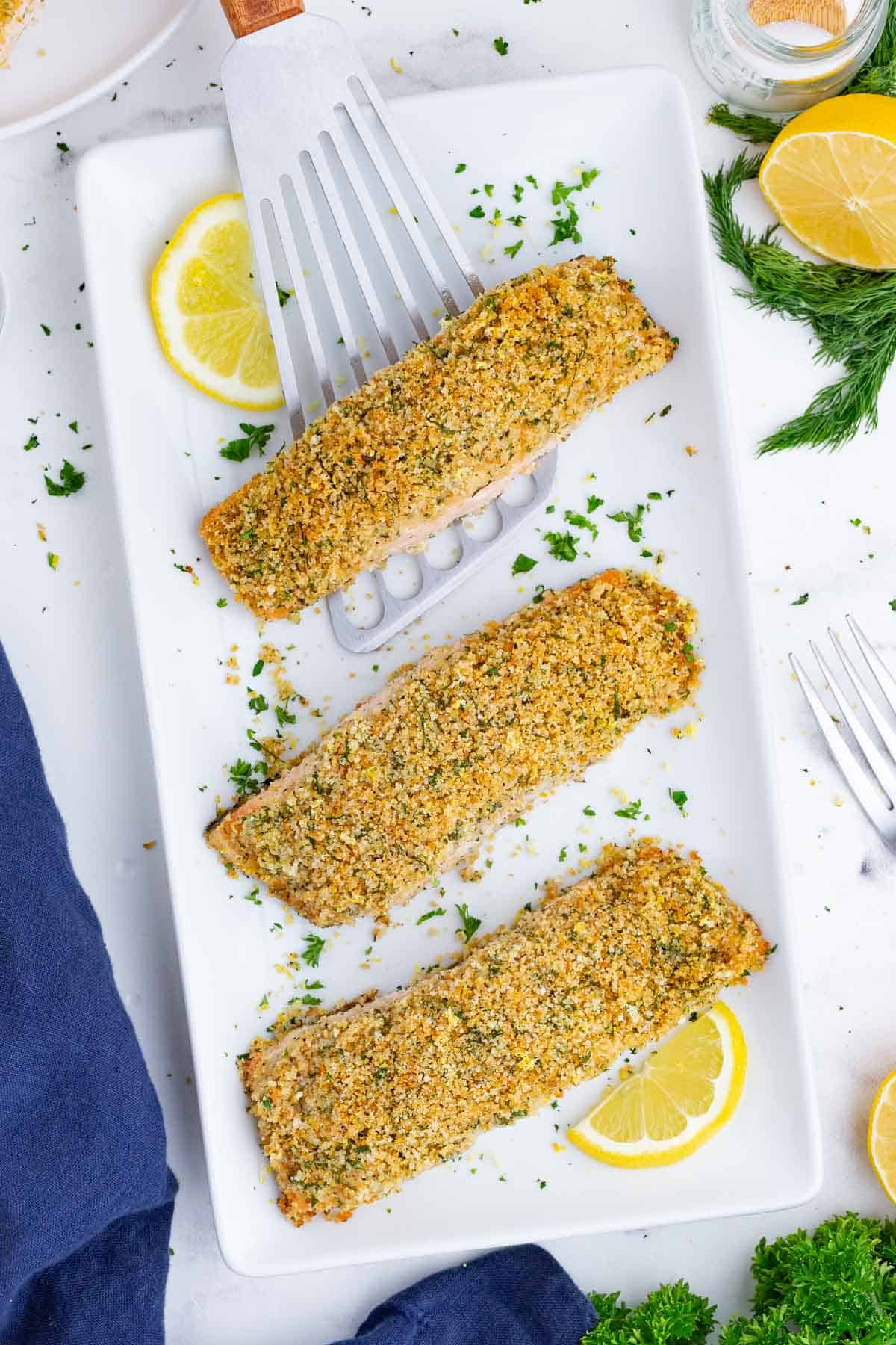 Four salmon filets with panko breadcrumbs on top are spread on a serving dish.