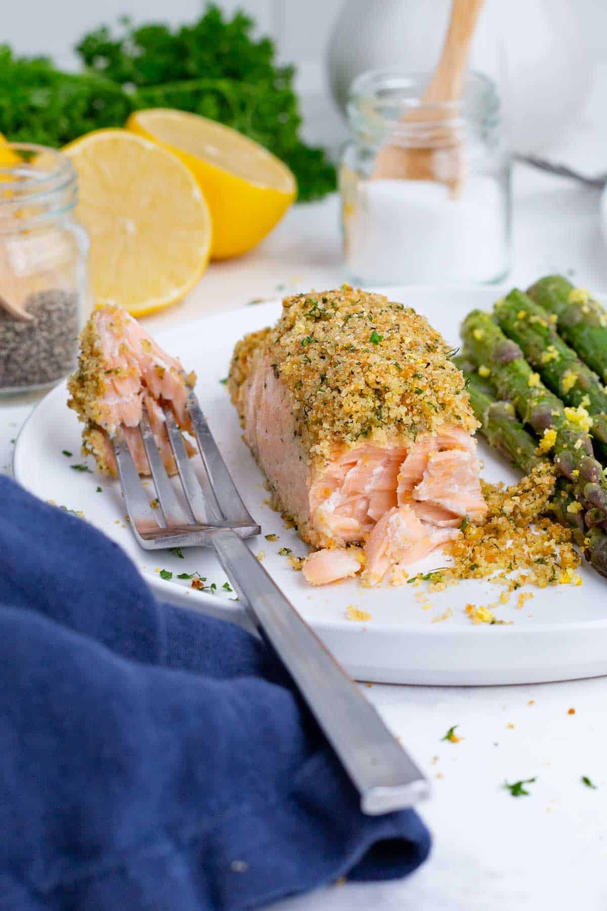 Crusted salmon served on a white plate with asparagus and a fork.