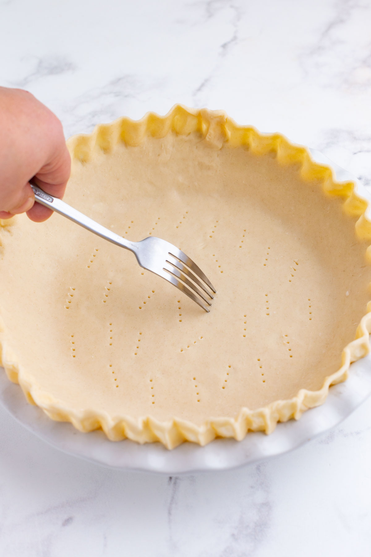 A fork pokes holes in the bottom of a pie crust.