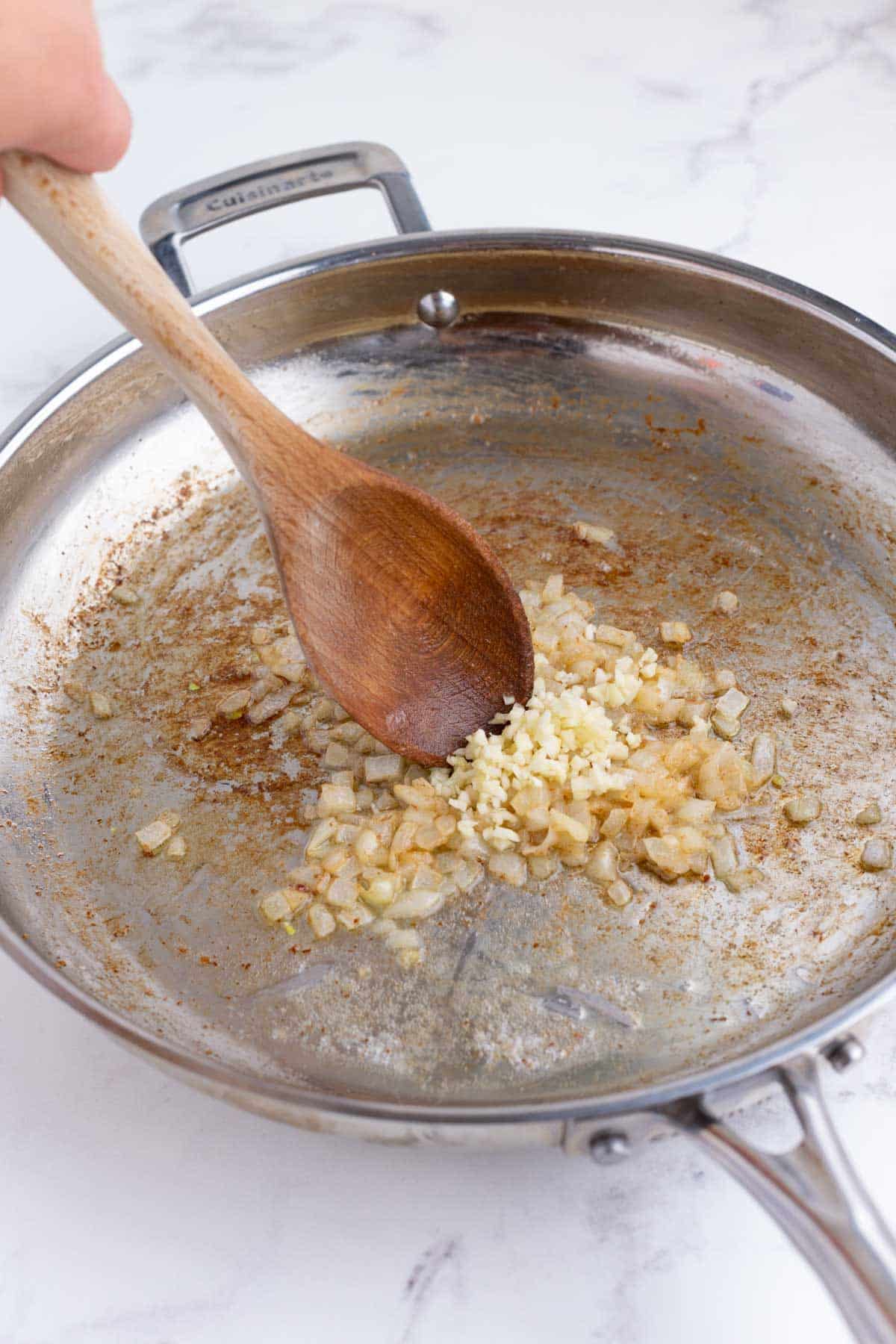 Onions and garlic are cooked in a skillet.