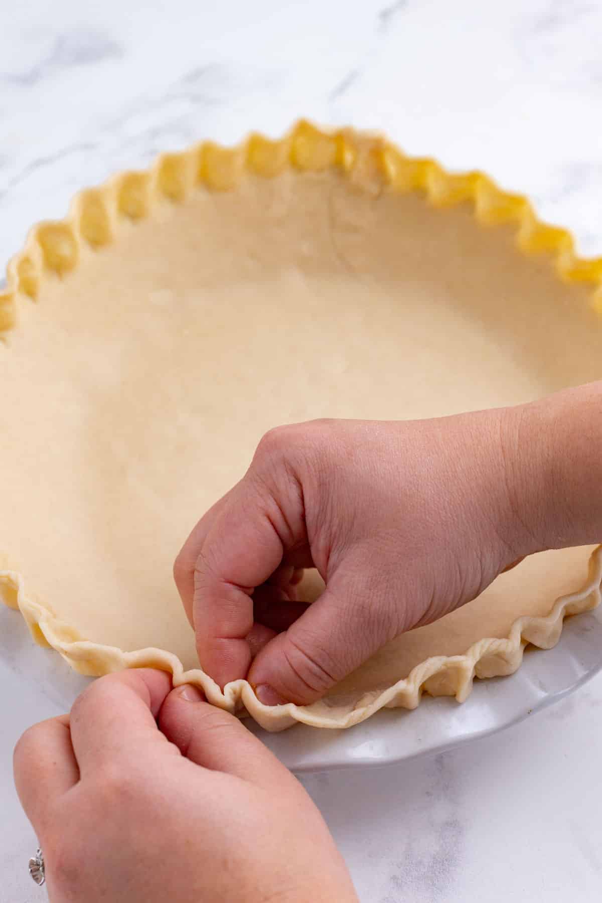 A hand crimps the edge of a pie crust.