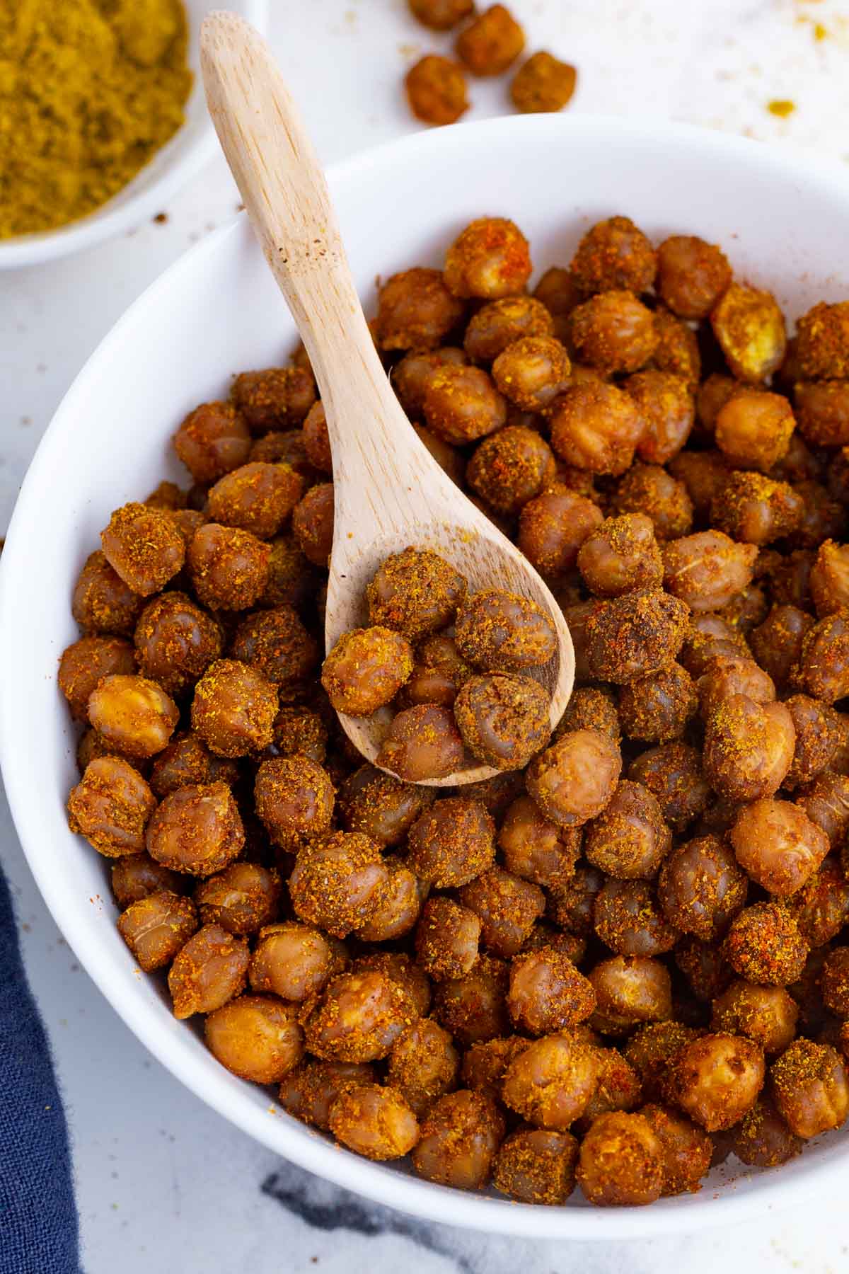A bowl roasted chickpeas are served in a bowl with a scoop.