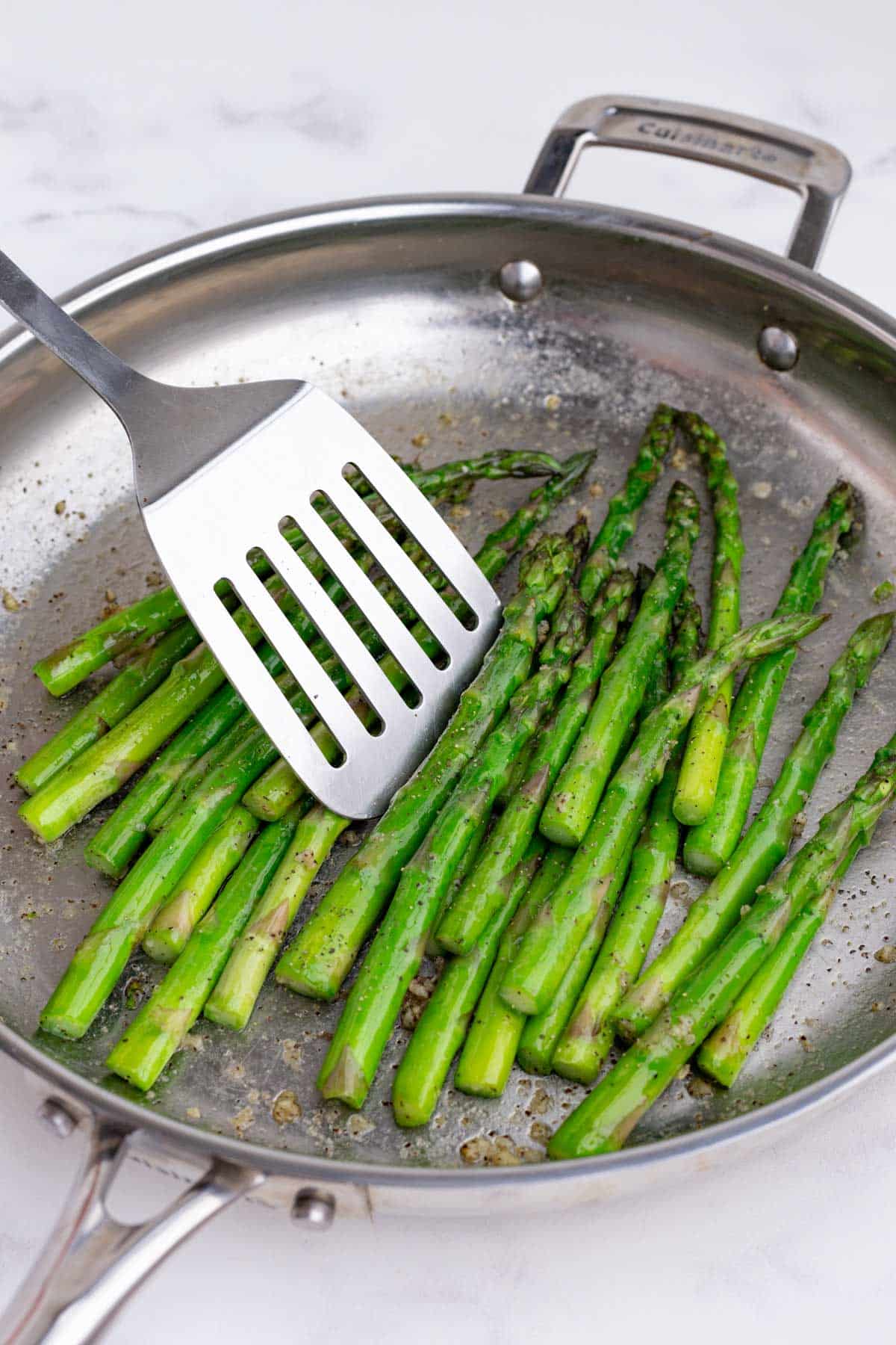 A spatula stirs the asparagus.