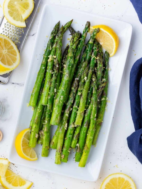 Air Fryer Asparagus is on a white plate with lemon wedges.