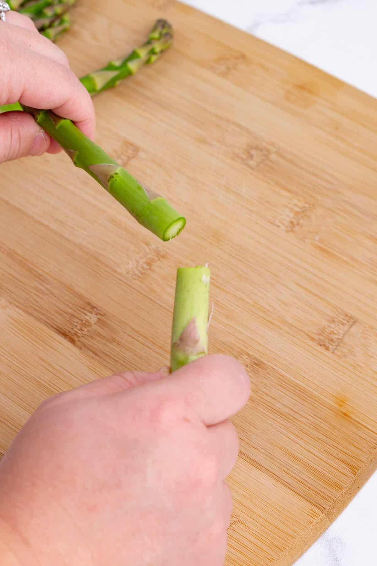 Hands remove the ends of the asparagus spears.