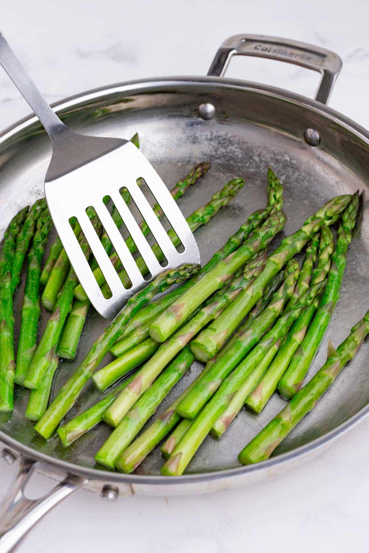 A spatula flips the asparagus.