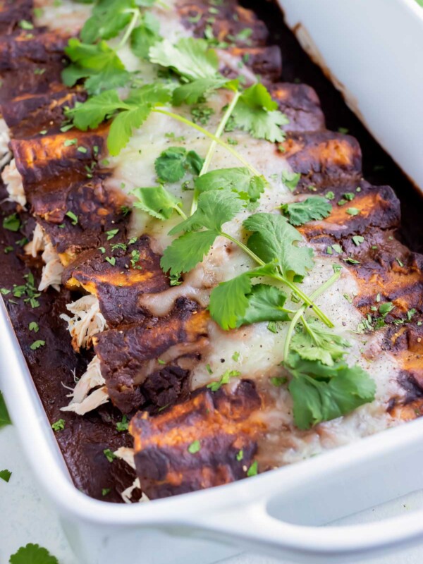 Chicken enchiladas smothered in mole sauce are shown in a casserole pan.