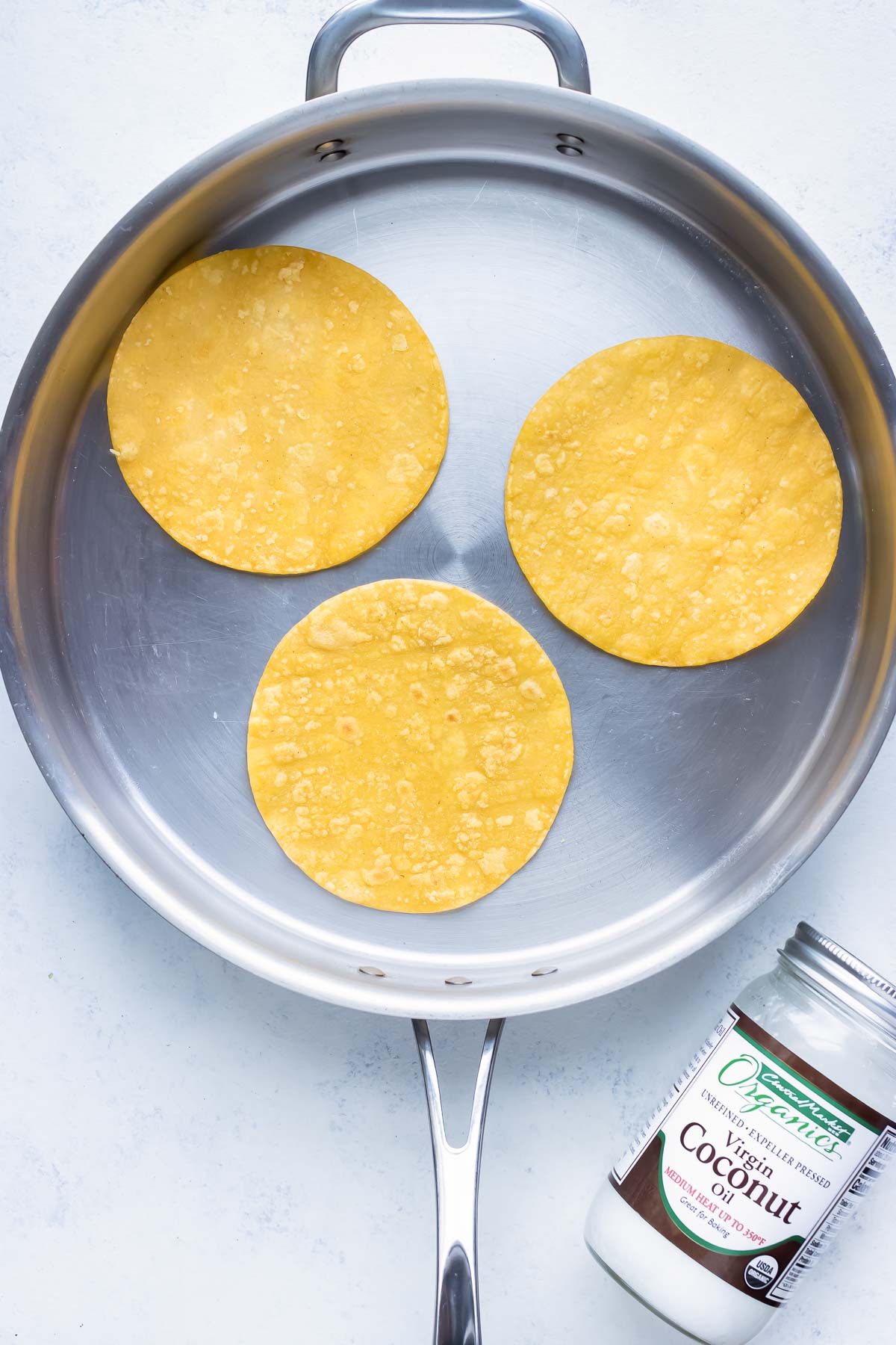 Corn tortillas are toasted in a pan.