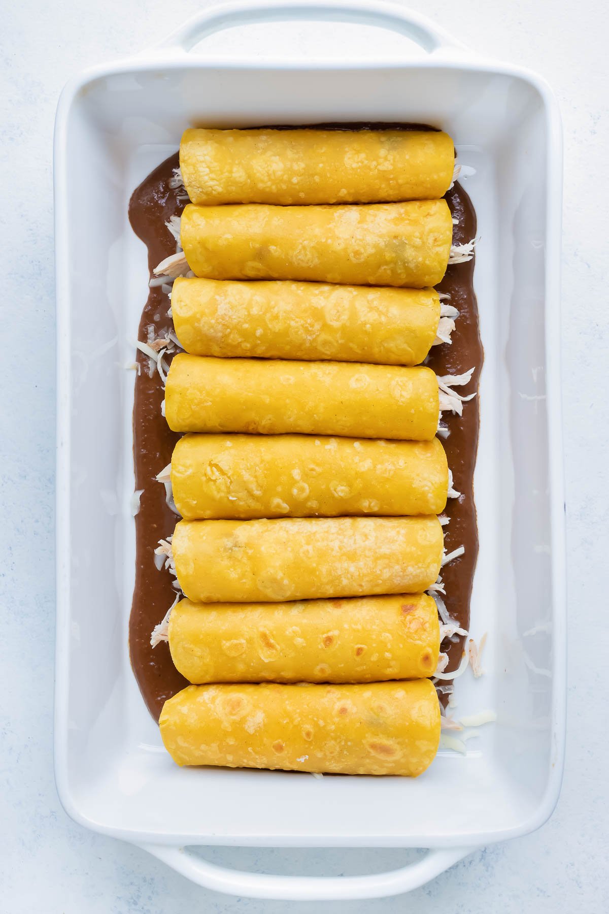 Rolled chicken filled tortillas are placed side by side in the pan.