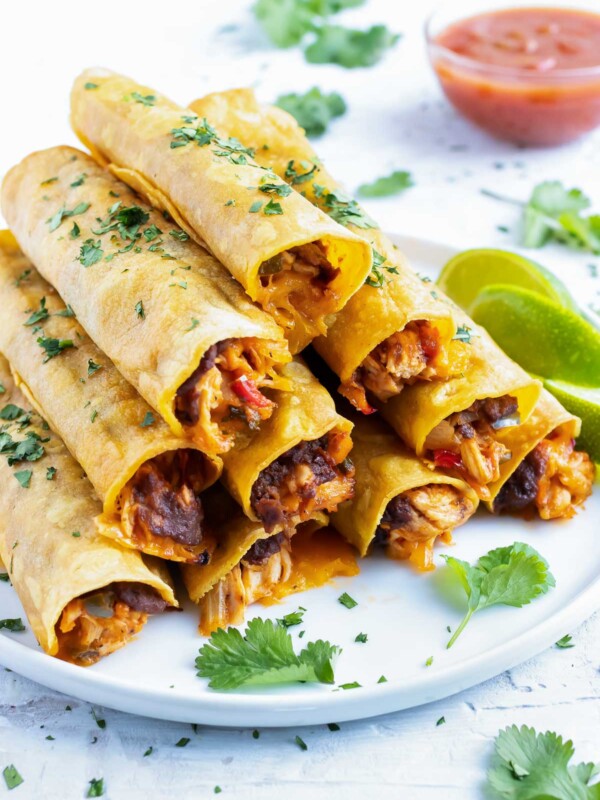 A stack of baked chicken taquitos with refried beans and cheese on a white plate for a Cinco de Mayo party.