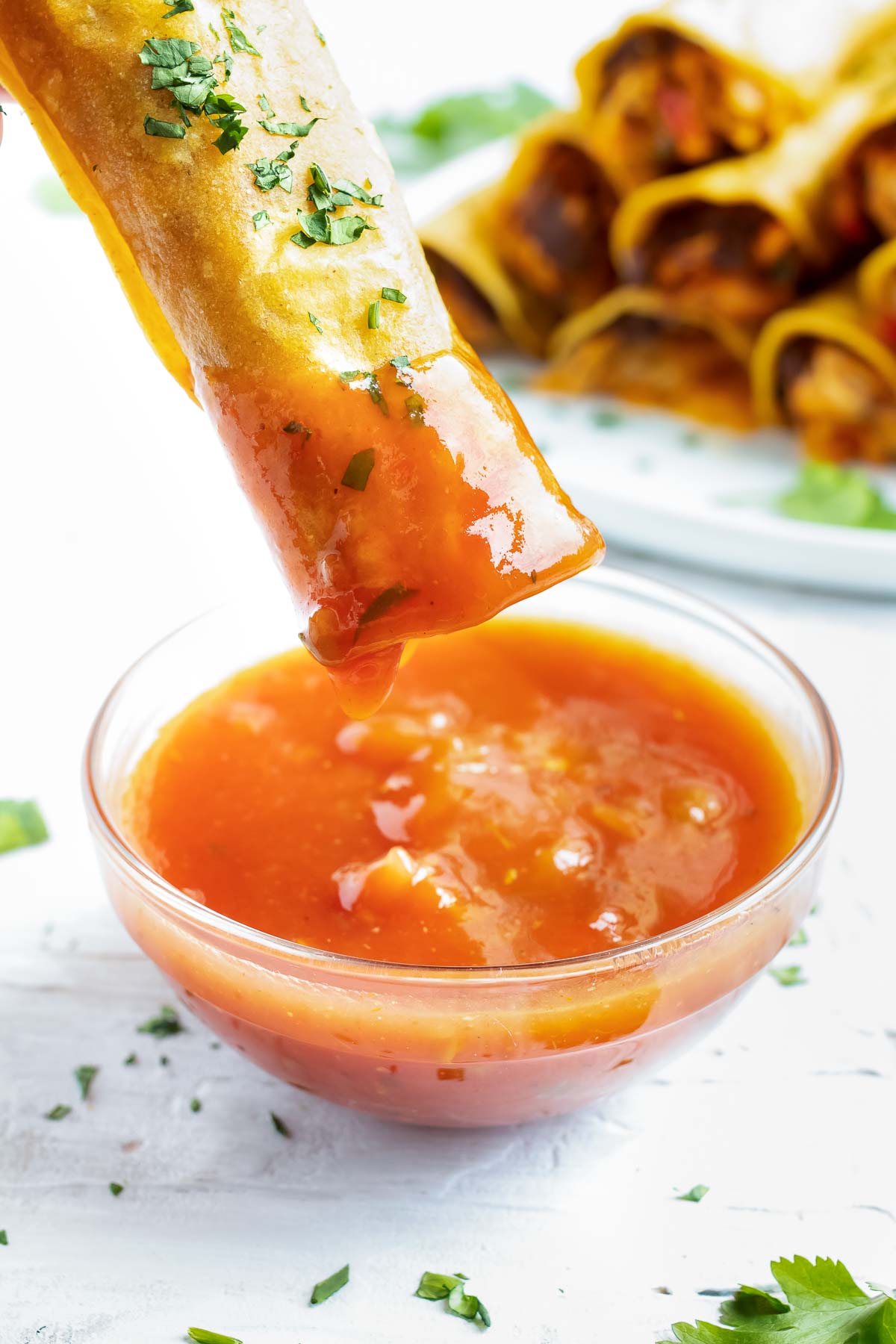 A baked chicken taquito being dipped into a glass bowl of salsa.