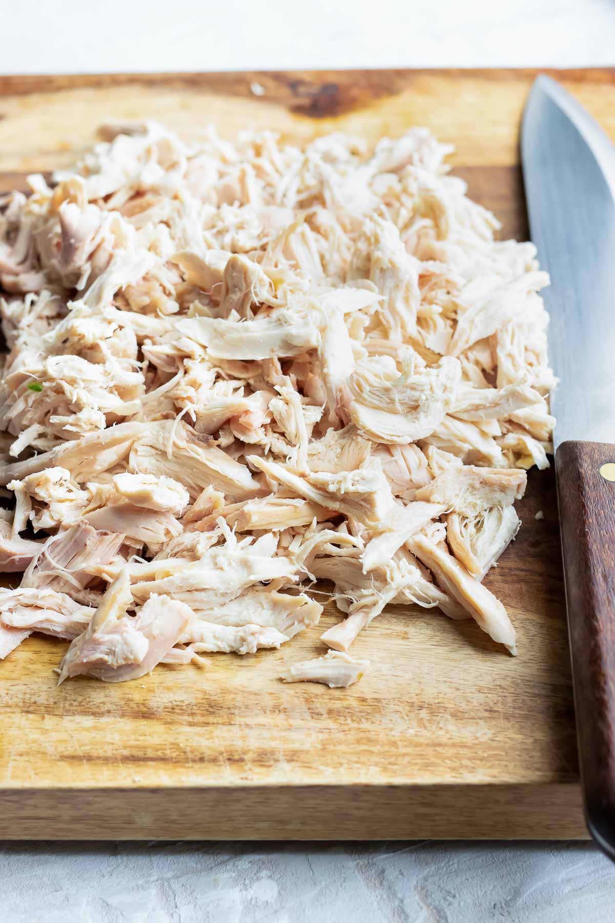 Shredded rotisserie chicken on a wooden cutting board for a chicken taquitos recipe.