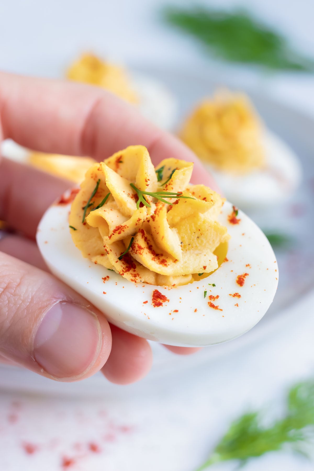 A hand picking up a hard-boiled egg with a creamy yolk filling with a fresh dill sprig on top.
