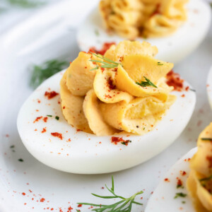Classic deviled egg recipe with paprika and fresh dill on a white serving plate.