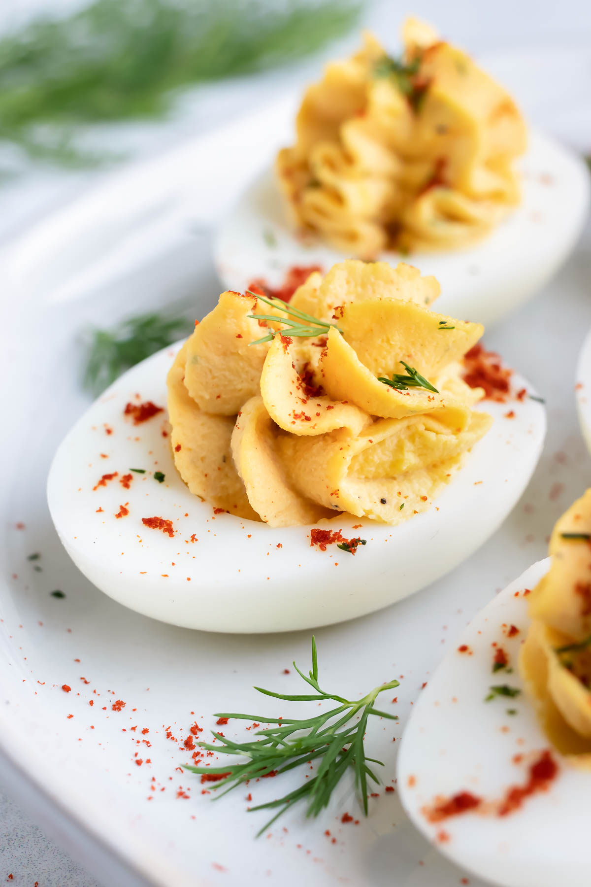 Classic deviled egg recipe with paprika and fresh dill on a white serving plate.