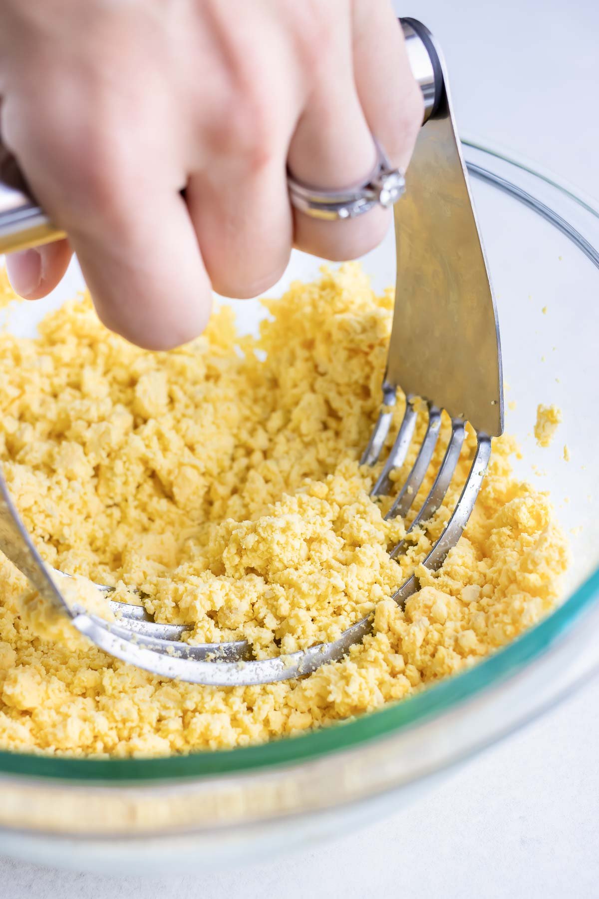 A pastry cutter is used to smooth out the egg yolks.