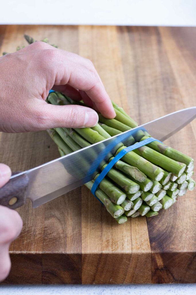 A sharp knife cutting through one bunch of asparagus.
