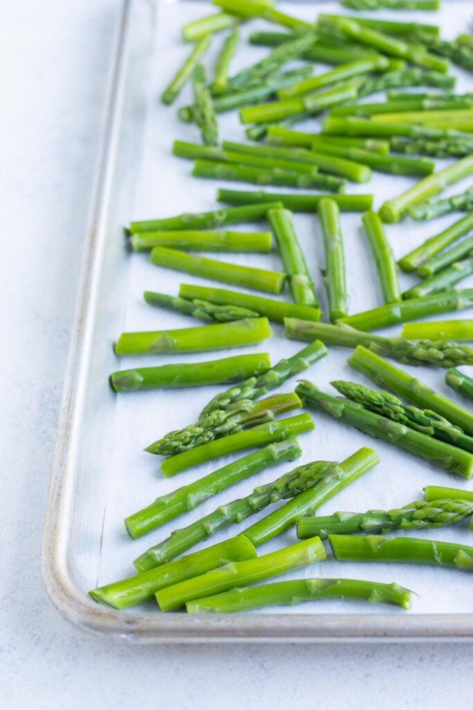 Cut up asparagus scattered on a sheet pan with parchment paper.