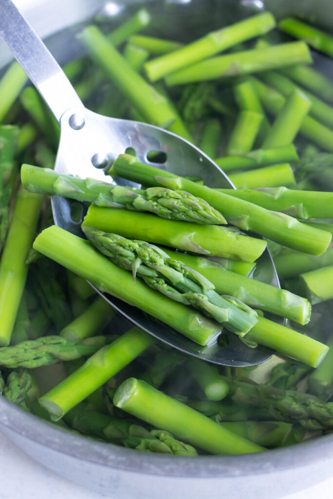 Cut up asparagus in a large pot of water with a slotted spoon taking some out.