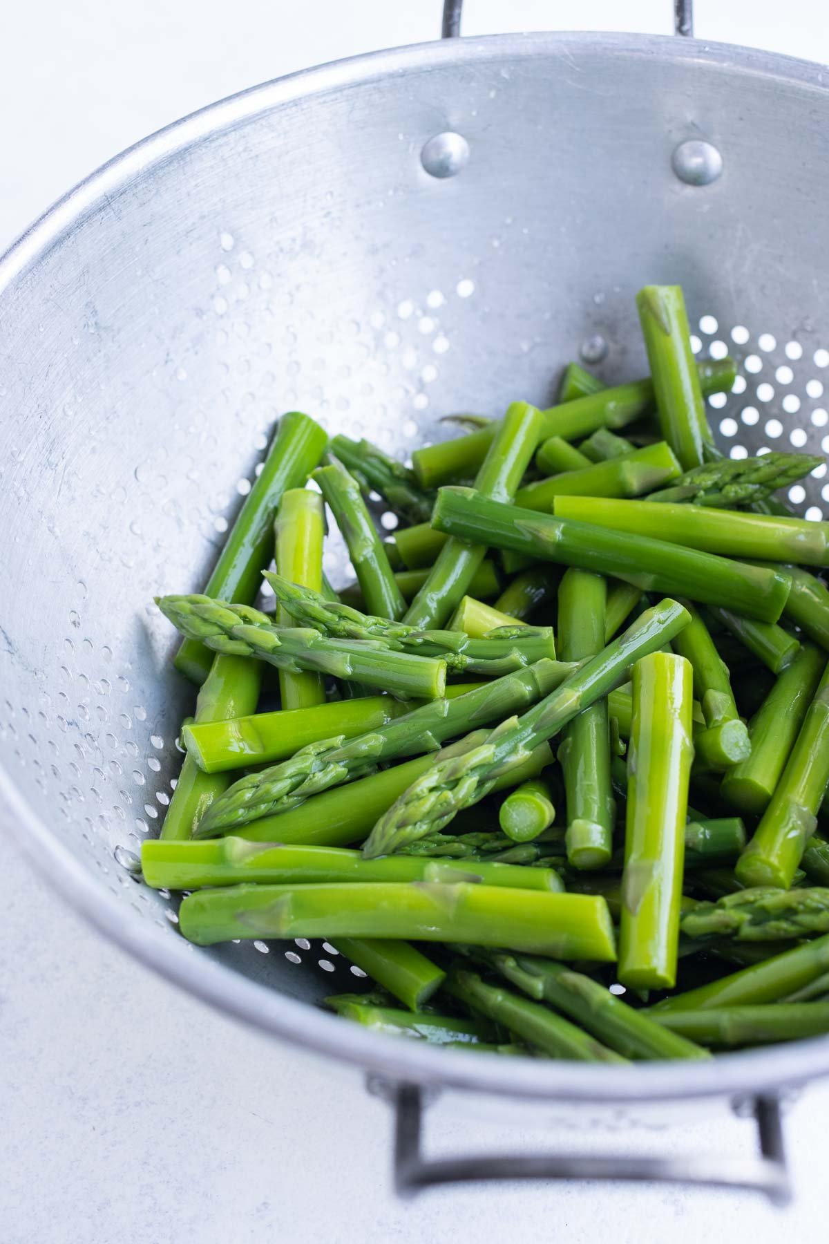 Cut asparagus sitting in a silver colander.