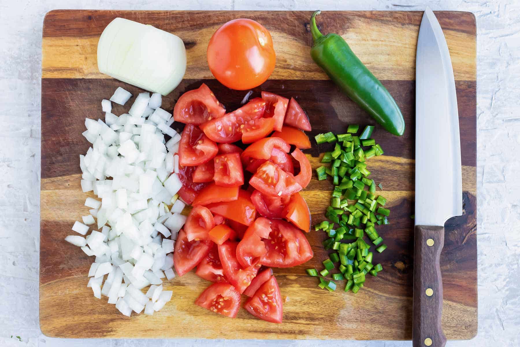 Diced onion, fresh tomatoes, and jalapenos that are chopped on a wooden cutting board.