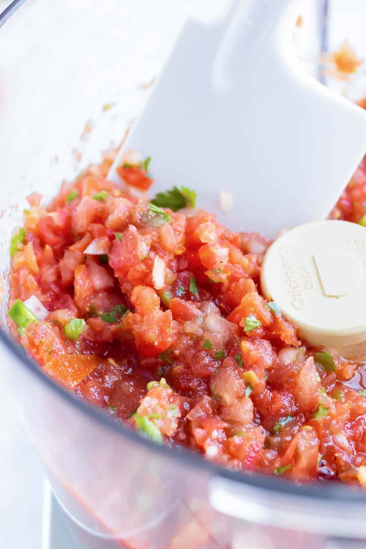 A white spatula scooping out fresh homemade salsa from a clear bowl.