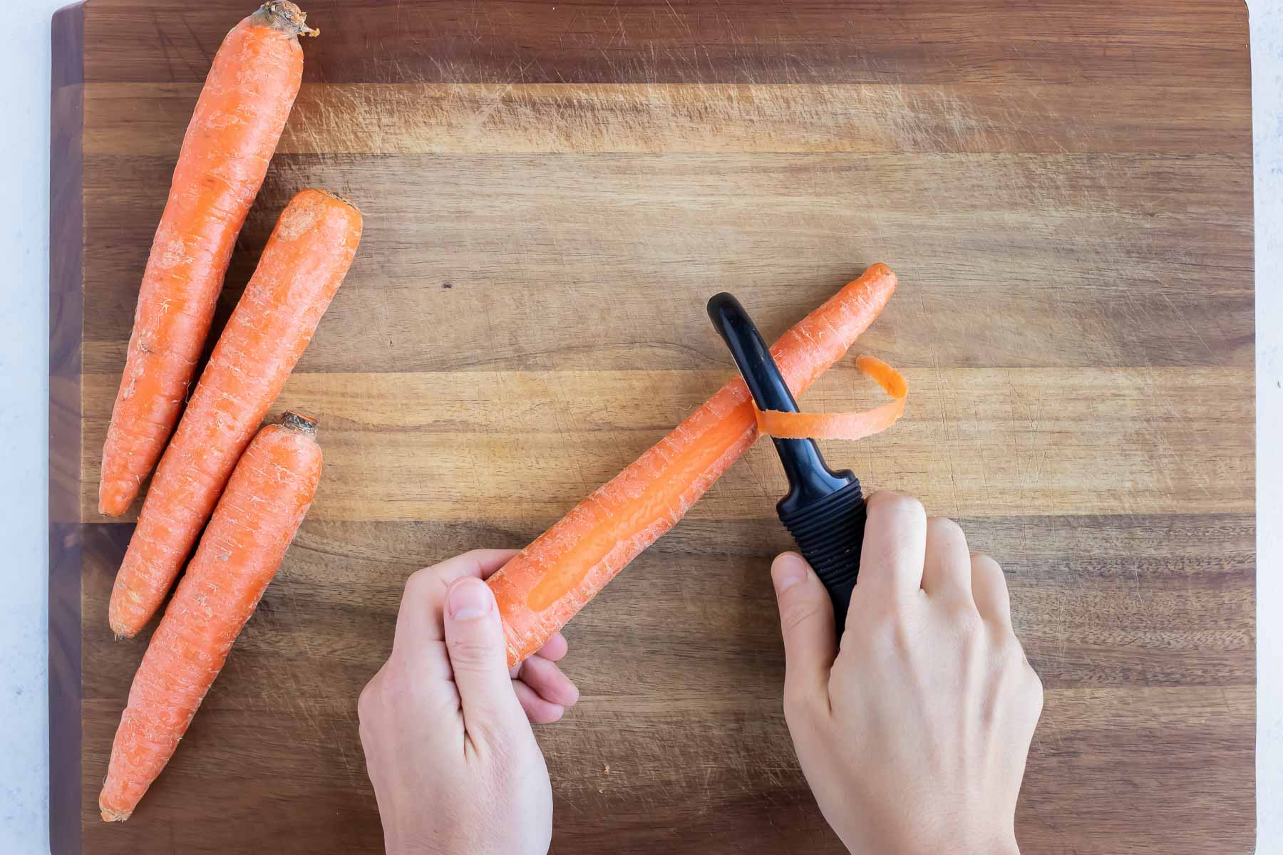 A raw carrot is peeled on a cutting board.
