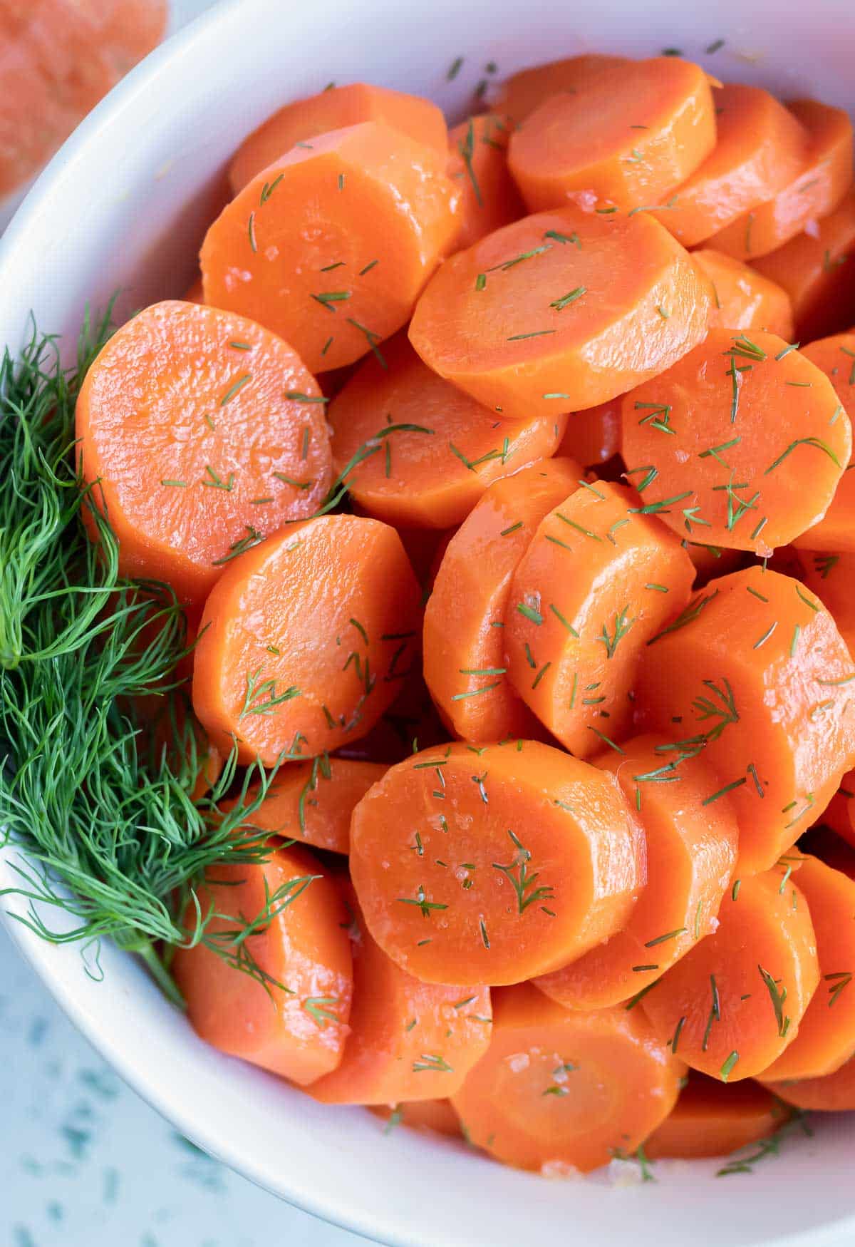 Sliced and seasoned boiled carrots are served in a white bowl with fresh dill.