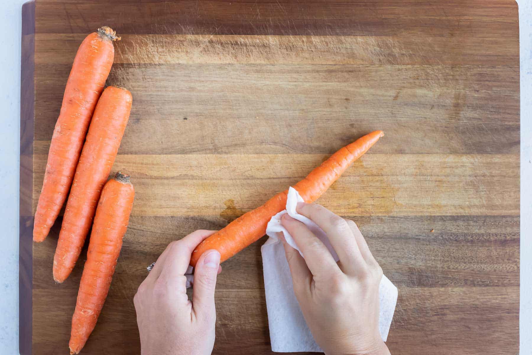 A whole carrot is cleaned with a paper towel.