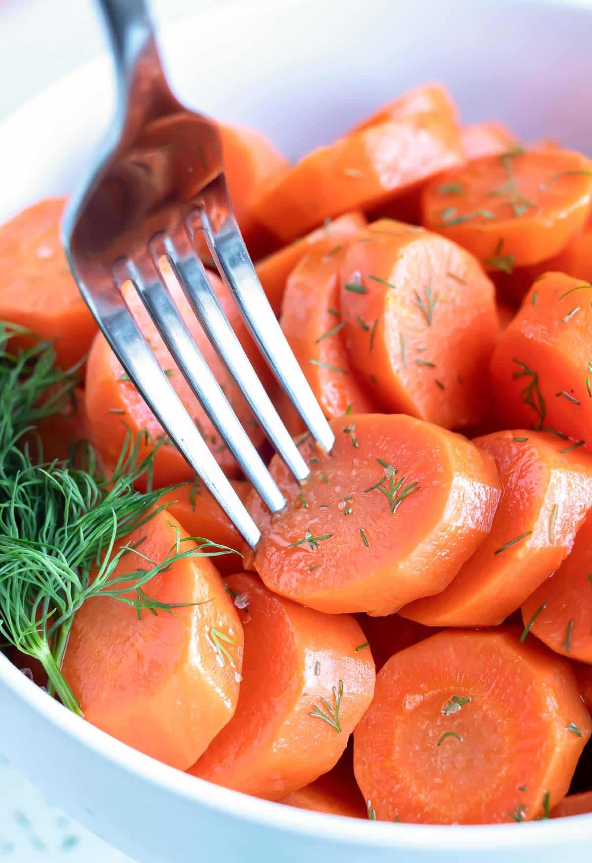 A sliced boiled carrot is being picked up from a bowl with a fork.