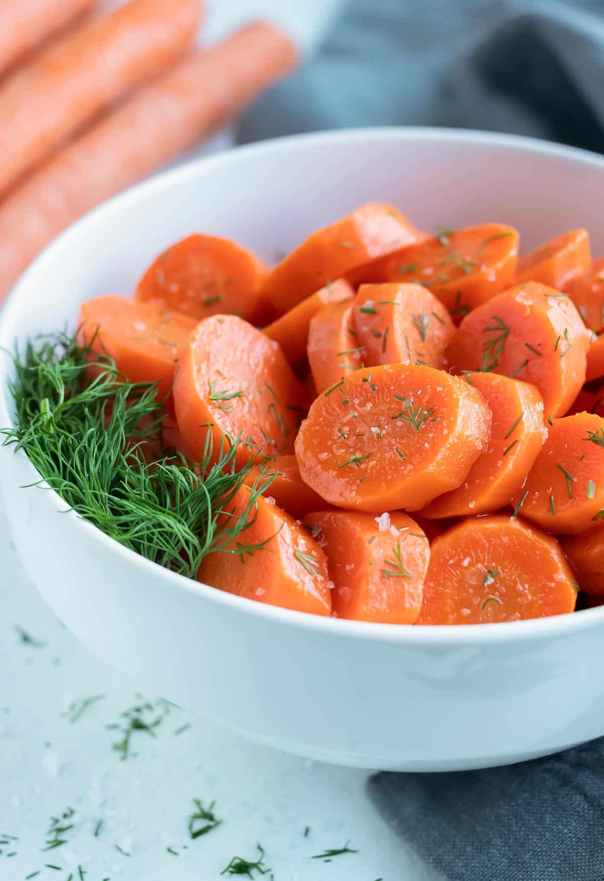 A bowl of sliced boiled carrots are served with fresh herbs.
