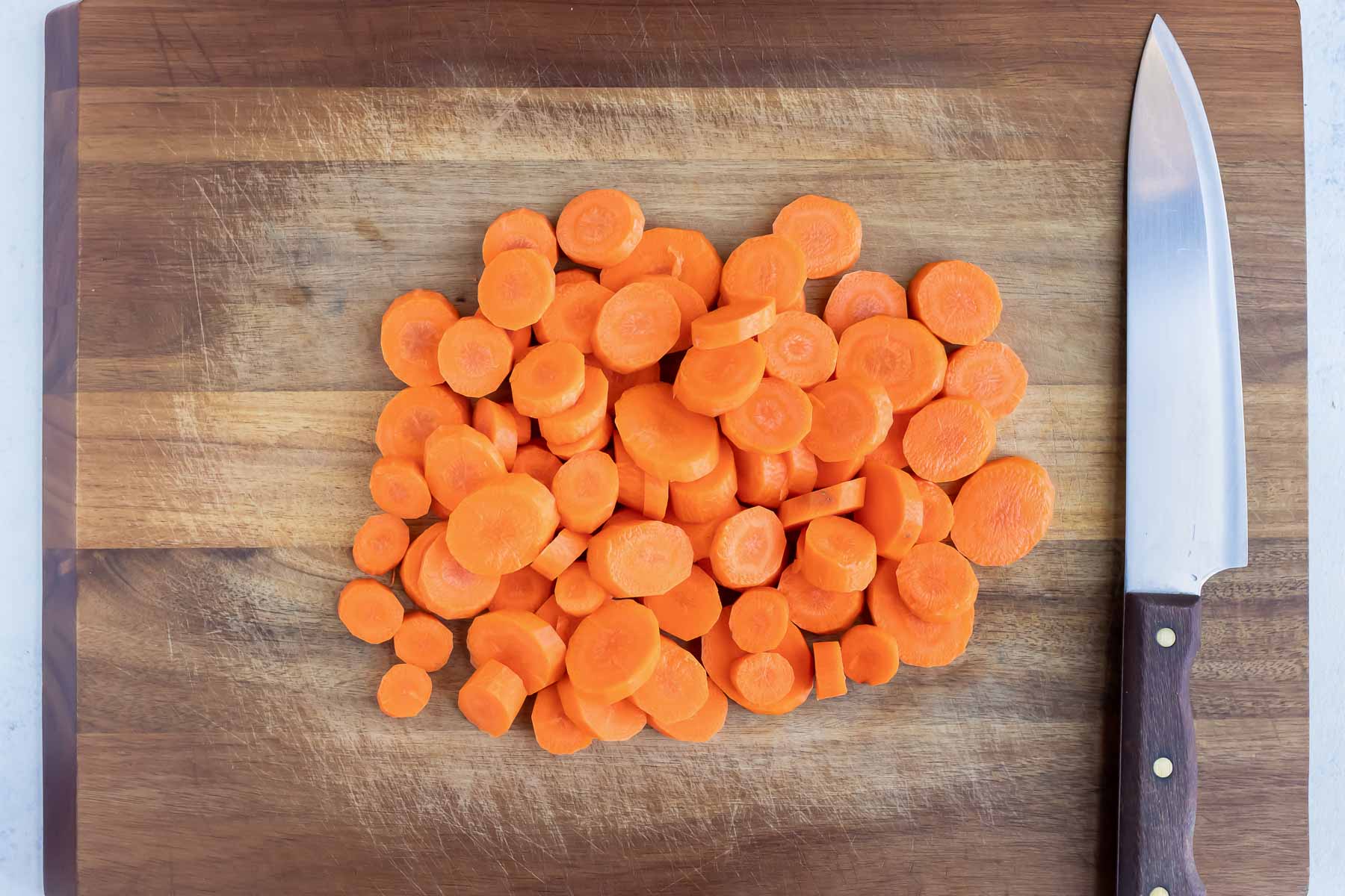 Sliced carrots are set in a pile on a cutting board.
