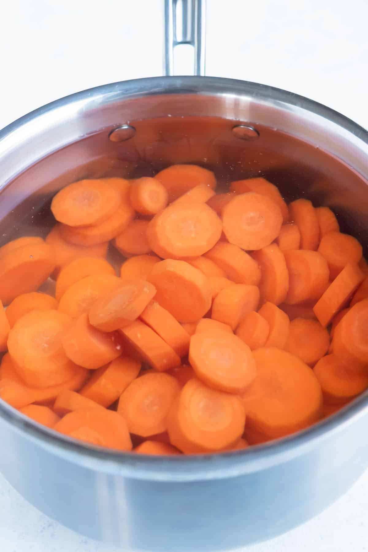 Sliced carrots are complete submerged in boil water in a pot.