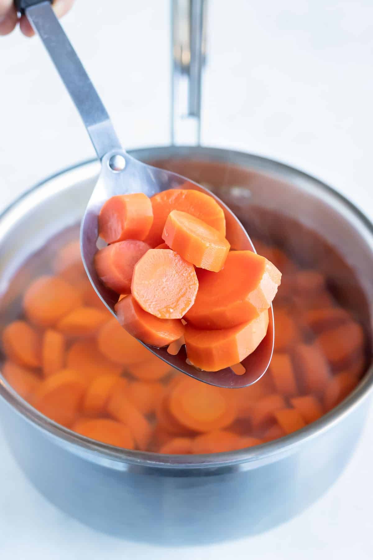 A spoon lifts boiled carrots out of a pot.