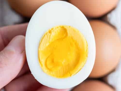 A hand is shown holding a hard-boiled egg with more eggs behind it.