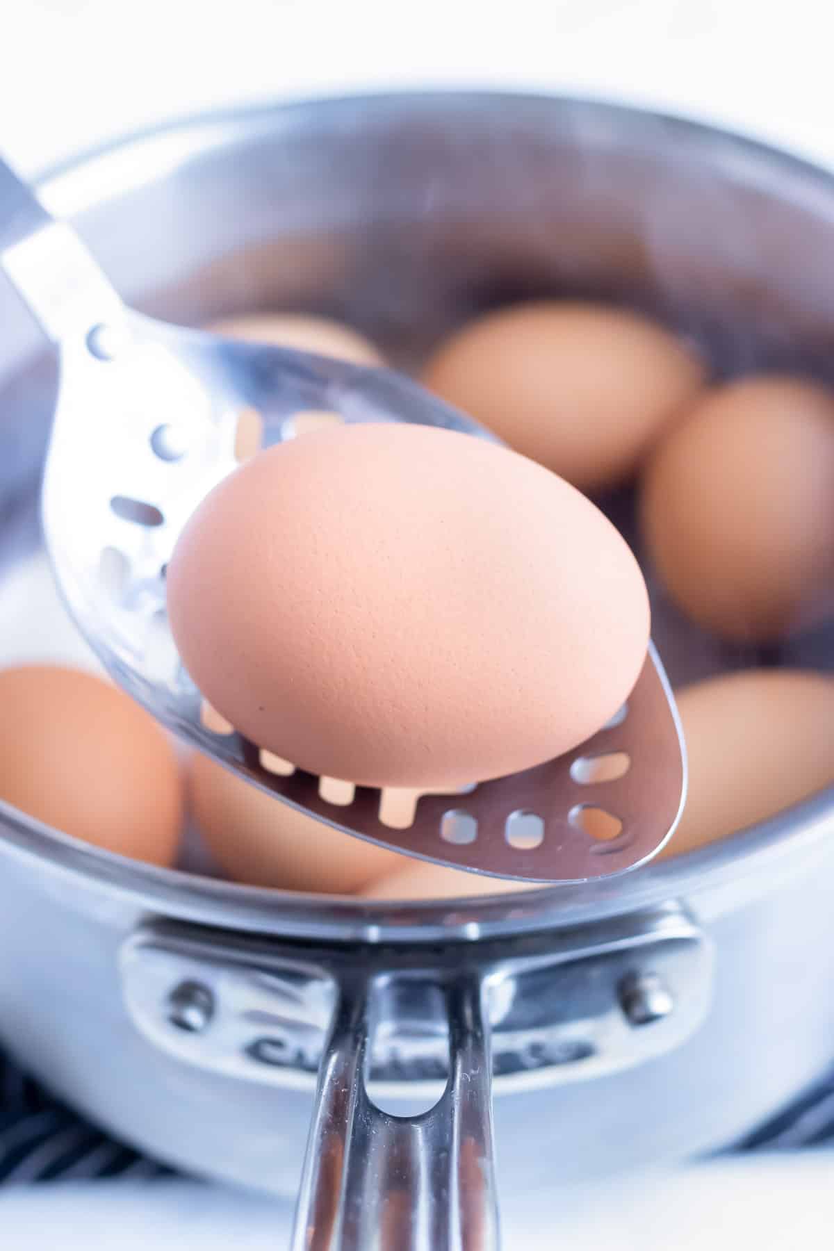 A slotted spoon is used to lift an egg out of the water.