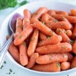 Glazed carrots made in the pressure cooker are served in a white bowl with a spoon.